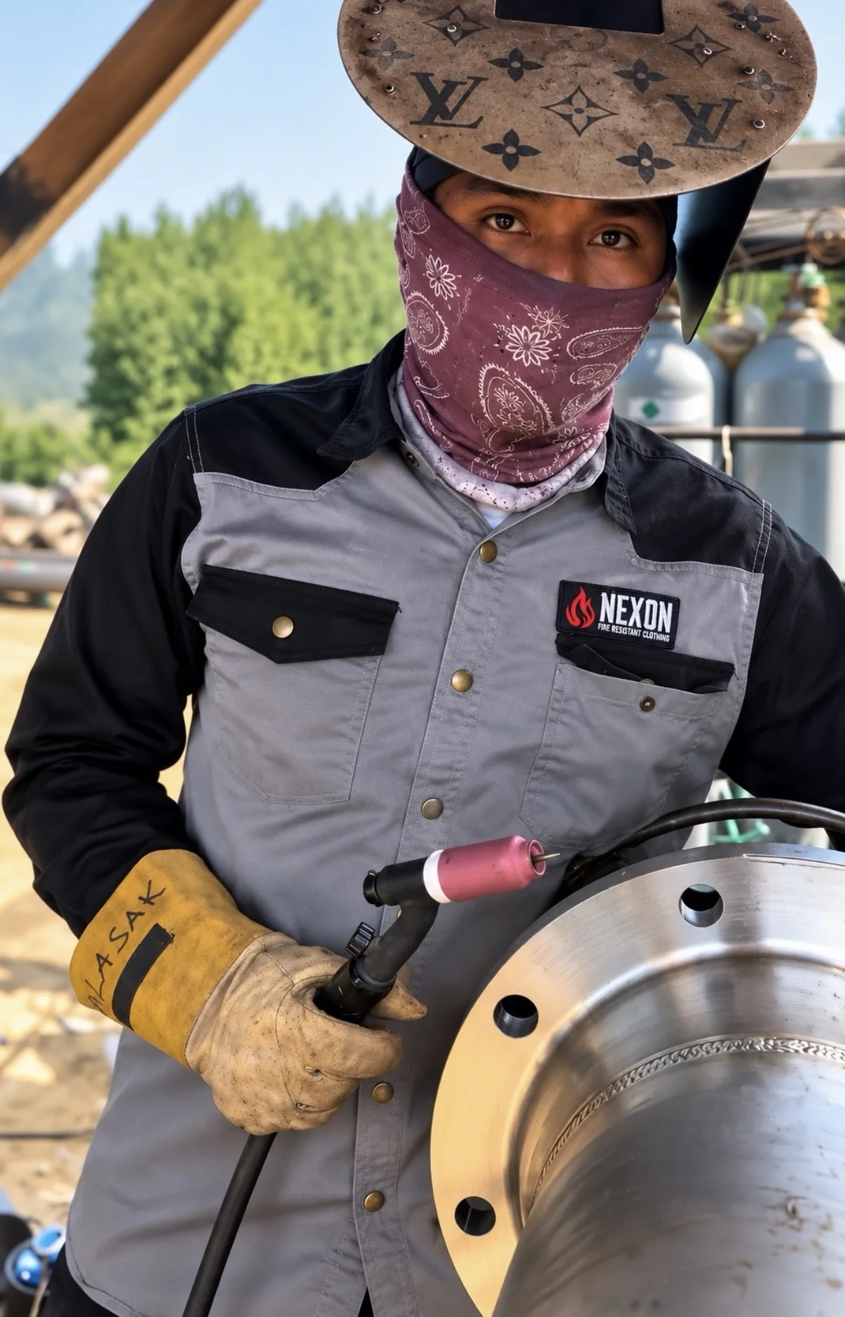 Welder wearing Næxon gray and black FR pearl snap shirt while TIG welding industrial pipe
