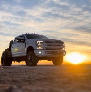 Lifted white pickup truck photographed from a low angle at sunset.