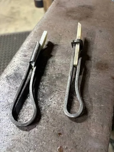 Two handmade metal holders containing rectangular white soapstone sticks on a steel workbench.